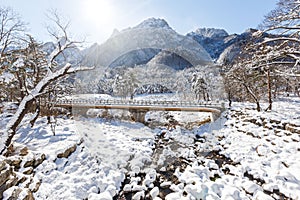 A pedestrian bridge over a frozen river against a background of high snowy rocks. Beautiful winter landscape