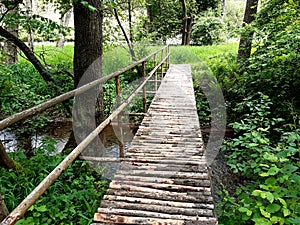 Pedestrian bridge over a stream built of wooden logs with a one-sided railing