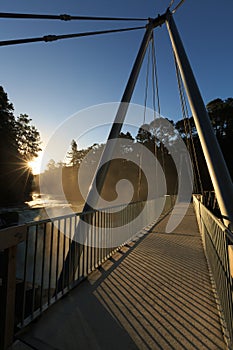 Pedestrian bridge over waterfall at sunset