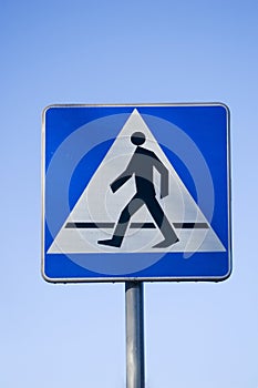 Pedestrian crossing sign isolated against blue sky.