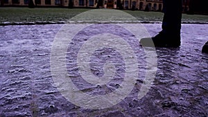 Pedestrian`s feet walk cautiously along the sidewalk covered with slippery ice. Winter weather is surprising.