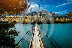 Pedestrian suspended wooden bridge over mountain river. Long bridge across the river against background of mountains covered with