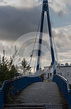 Pedestrian suspension bridge in blue. Against the background of the cloudy sky.