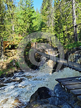 Pedestrian suspension bridge over the Ahvenkoski waterfall on the Tokhmayoki River in Karelia on a clear summer morning
