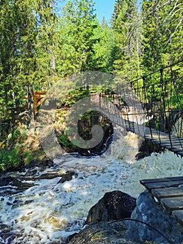 Pedestrian suspension bridge over the Ahvenkoski waterfall on the Tokhmayoki River in Karelia on a clear summer morning