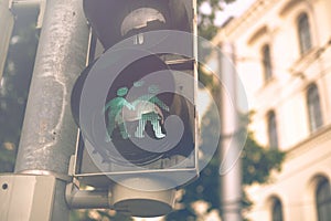 pedestrian traffic light modified for a LGBTQ event shows a green graphic of a loving different sex couple in a city surrounding