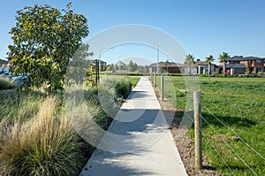 A pedestrian walkway/footpath leads to a residential neighbourhood with some modern Australian homes. Suburban view over a park