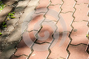 The pedestrian walkway is paved with red brick paving slabs, on it is a pattern of shadows from trees. texture, roughness