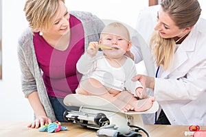 Pediatric care specialist smiling while measuring the weight of a baby girl