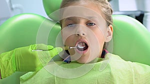 Pediatric dentist checking teeth with mouth mirror, routine dental examination