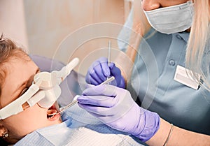 Pediatric dentist examining child teeth with dental explorer and mirror.