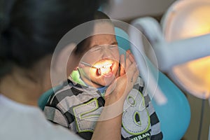 Pediatric dentist examining a little boys teeth in the dentists chair at the dental clinic. A child with a dentist in a dental
