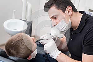 Pediatric dentist examining teeth of boy patient in dental clinic using dental tools - probe and mirror