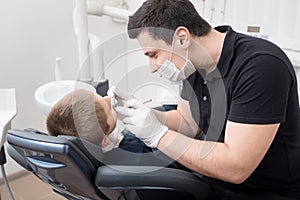 Pediatric dentist examining teeth of boy patient in dental clinic using dental tools - probe and mirror