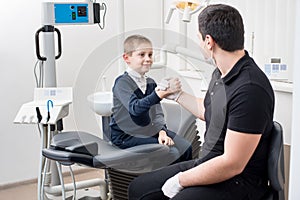 Pediatric dentist shake hands with young boy, congratulate patient for a successful treatment in dental office