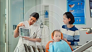 Pediatric dentist showing teeth x-ray on tablet pc computer screen to mother