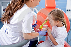Pediatric dentist shows how to properly brush a little girl`s teeth. A beautiful girl is smiling in dentist`s office. concept is