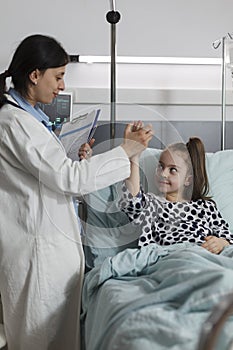 Pediatric expert doing high five gesture with ill kid sitting in patient bed