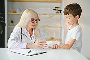 Pediatrician doctor bandaging child's arm. Broken arm in a boy.