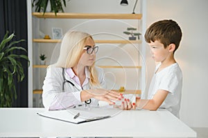 Pediatrician doctor bandaging child's arm. Broken arm in a boy.