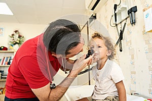 Pediatrician doctor examining child. Male doctor examining boy's ear with otoscope in hospital.