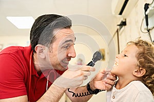 Pediatrician doctor examining child. Male doctor examining boy's ear with otoscope in hospital.