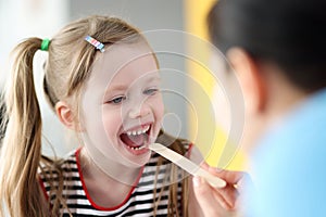 Pediatrician doctor examining throat of little girl with spatula