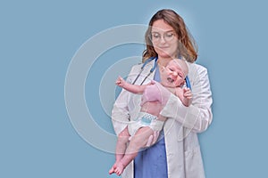 Pediatrician doctor holding newborn baby and smiling, blue studio background. Happy nurse in uniform with a baby in her arms