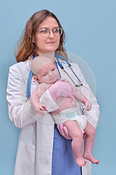 Pediatrician doctor holding newborn baby and smiling, blue studio background. Happy nurse in uniform with a baby in her arms
