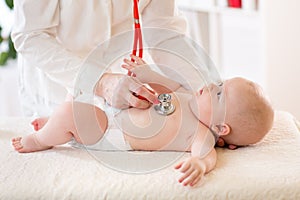 Pediatrician examines baby using stethoscope to listen to baby`s chest checking heart beat. Child is looking at doctor