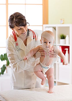 Pediatrician examining cute baby boy. Doctor testing walking reflex