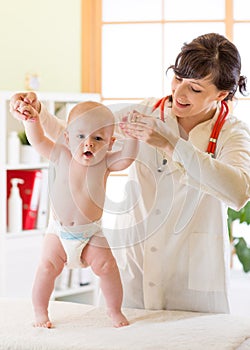 Pediatrician examining cute baby boy and testing his walking reflex
