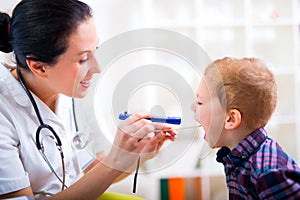 Pediatrician examining little boy's throat with tongue depressor