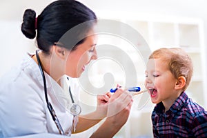 Pediatrician examining little boy's throat with tongue depressor