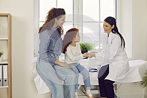 Pediatrician holds hand of child assuring her that there is nothing to fear during medical exam.