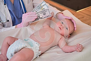 A pediatrician keeps money in dollars for paying for the treatment of a newborn baby. A doctor in uniform with money for a visit