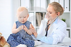 Pediatrician is taking care of baby in hospital. Little girl is being examine by doctor with stethoscope