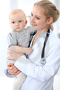 Pediatrician is taking care of baby in hospital. Little girl is being examine by doctor with stethoscope