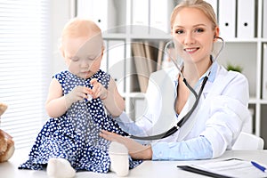 Pediatrician is taking care of baby in hospital. Little girl is being examine by doctor with stethoscope