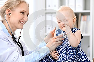 Pediatrician is taking care of baby in hospital. Little girl is being examine by doctor with stethoscope