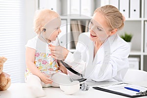 Pediatrician is taking care of baby in hospital. Little girl is being examine by doctor with stethoscope