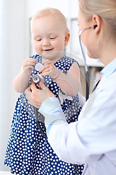 Pediatrician is taking care of baby in hospital. Little girl is being examine by doctor with stethoscope