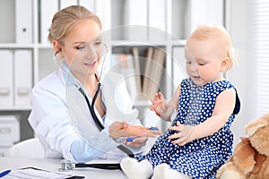 Pediatrician is taking care of baby in hospital. Little girl is being examine by doctor with stethoscope