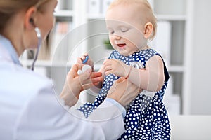 Pediatrician is taking care of baby in hospital. Little girl is being examine by doctor with stethoscope