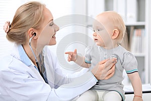 Pediatrician is taking care of baby in hospital. Little girl is being examine by doctor with stethoscope