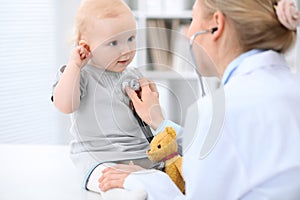 Pediatrician is taking care of baby in hospital. Little girl is being examine by doctor with stethoscope