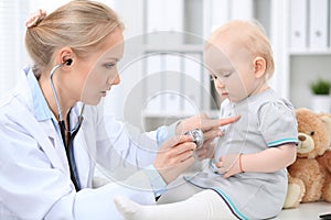 Pediatrician is taking care of baby in hospital. Little girl is being examine by doctor with stethoscope