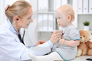 Pediatrician is taking care of baby in hospital. Little girl is being examine by doctor with stethoscope