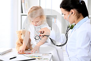 Pediatrician is taking care of baby in hospital. Little girl is being examine by doctor with stethoscope. Health care