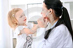 Pediatrician is taking care of baby in hospital. Little girl is being examine by doctor with stethoscope. Health care